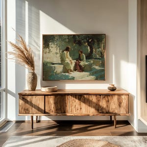 May include: A living room scene featuring a large wooden cabinet with four doors, a framed painting depicting two figures, and decorative items. The cabinet is made of light-colored wood and has a minimalist design. A vase with tall, dried plants sits on the cabinet.