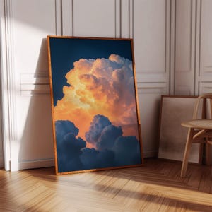 Peut inclure: Une impression encadrée représentant un paysage nuageux spectaculaire. L'œuvre présente un affichage vibrant de nuages orange et bleus sur un ciel bleu foncé. Le cadre en bois complète les tons chauds des nuages, créant un contraste visuel saisissant.