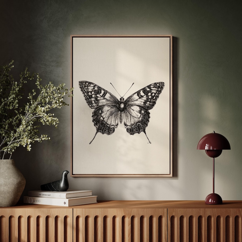 Pu&ograve; includere: Un'illustrazione in bianco e nero di una farfalla con le ali spiegate. La farfalla &egrave; centrata su una tela color crema con una cornice in legno.