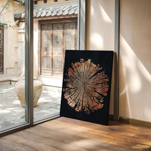 May include: A black canvas print featuring a detailed, copper-colored cross-section of a tree trunk. The artwork is leaning against a wall in a room with a wooden floor and a view of an outdoor courtyard.