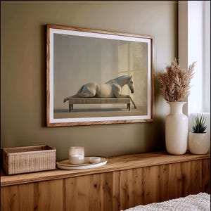 May include: A framed art print featuring a white horse reclining on a bench. The artwork is set in a room with a neutral color palette and a wooden frame. The print is displayed above a wooden shelf with decorative items.