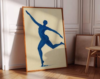 May include: A framed art print featuring a blue silhouette of a dancer in motion. The artwork is set against a cream-colored background and framed in a warm wood tone. The print is leaning against a white wall.