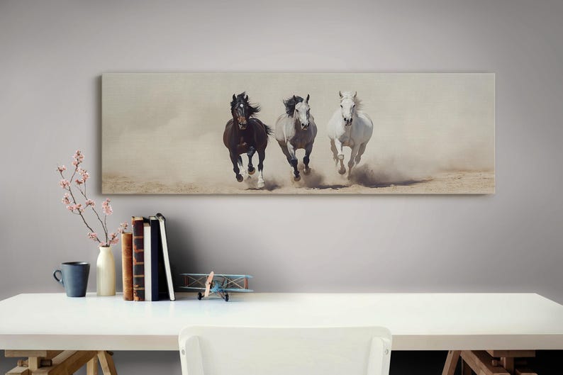 May include: A canvas print featuring three horses galloping across a dusty landscape. The horses are a dark brown, gray, and white, with their manes and tails flowing in the wind. The artwork is rectangular and mounted on a wall.