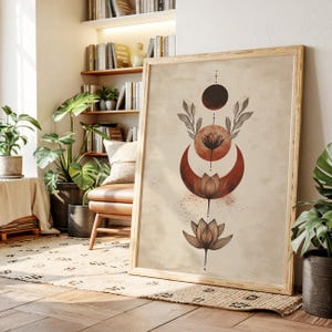 Op de afbeelding: Een ingelijste kunstdruk met een hemels ontwerp. Het toont een lotusbloem, een halve maan en een zon in bruine en roesttinten. Het kunstwerk heeft een beige achtergrond en zit in een licht houten frame. De print leunt tegen een muur in een kamer met planten.