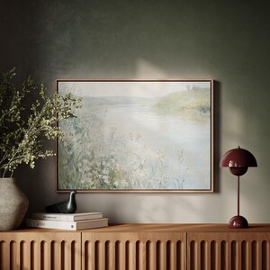 K&ouml;nnte beinhalten: Ein gerahmtes Gem&auml;lde einer Landschaft mit einem Fluss und gr&uuml;nen H&uuml;geln im Hintergrund. Das Gem&auml;lde h&auml;ngt an einer Wand &uuml;ber einem Holzschrank mit einer roten Lampe auf der rechten Seite.