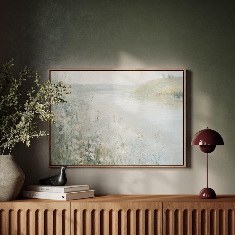 K&ouml;nnte beinhalten: Ein gerahmtes Gem&auml;lde einer Landschaft mit einem Fluss und gr&uuml;nen H&uuml;geln im Hintergrund. Das Gem&auml;lde h&auml;ngt an einer Wand &uuml;ber einem Holzschrank mit einer roten Lampe auf der rechten Seite.