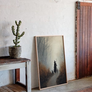 May include: A framed art print depicts a witch with a cat walking down a path in a misty forest. The artwork is in a light wood frame, leaning against a white wall. A cactus in a textured pot sits on a rustic wooden table.