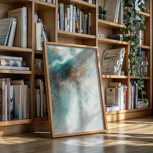 Pu&ograve; includere: Una stampa artistica astratta incorniciata con una cornice in legno. L'opera presenta una miscela di colori verde acqua, bianco e oro, creando un effetto strutturato simile all'acquerello. La stampa &egrave; appoggiata a una libreria in legno piena di libri.