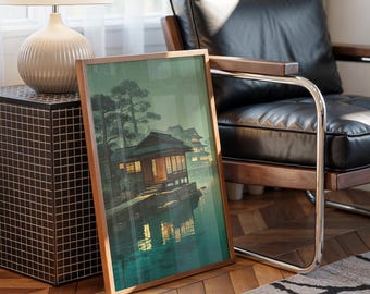 Può includere: Una stampa incorniciata di un paesaggio giapponese con edifici tradizionali su un lago, con alberi e riflessi. L'opera d'arte ha una cornice in legno ed è appoggiata a una sedia. La tavolozza dei colori comprende verdi, marroni e illuminazione soffusa.