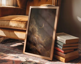 May include: A framed art print depicting a night sky with a crescent moon and clouds in brown, gold, and grey tones. The artwork is propped against a stack of books on a patterned rug. The frame is made of light-coloured wood.