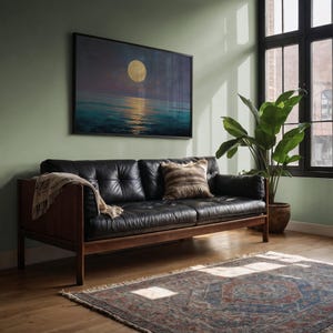 May include: A living room scene featuring a black leather sofa with wooden arms and legs. A framed artwork depicting a moonlit ocean hangs above the sofa. A patterned rug and a potted plant complete the room's decor.