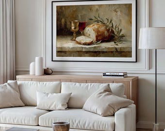 May include: A framed still life painting featuring a loaf of bread, a glass of red wine, and a golden chalice. The painting has a neutral color palette with olive branches and a slice of bread in the foreground. The artwork is displayed above a light-colored wooden cabinet.