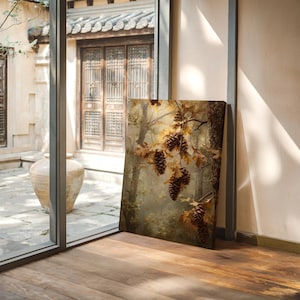 May include: A canvas print featuring a detailed painting of pine cones and autumn leaves. The artwork is set in a forest scene with warm, earthy tones of brown, gold, and green. The print is leaning against a window.