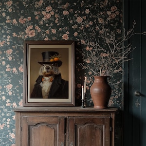 May include: A framed portrait of a groundhog in a top hat and formal attire, adorned with oranges. The artwork is displayed on a wooden cabinet, with a floral wallpaper backdrop. A vase with branches and lit candles complete the scene.