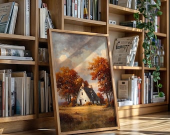 May include: A framed landscape painting of a white cottage with a thatched roof, set amidst autumn trees with vibrant orange and red foliage. The artwork is displayed on a wooden floor in front of a bookshelf.