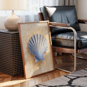 May include: A framed artwork featuring a light blue seashell sculpture. The artwork is set against a beige background and framed in wood. The image is in a room with a black leather chair, a side table, and a lamp.