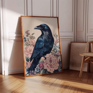 May include: A framed art print featuring a dark blue raven perched amidst a backdrop of pink and blue floral blooms. The raven's feathers are detailed with shades of blue. The artwork is displayed in a room with wooden floors and a chair.