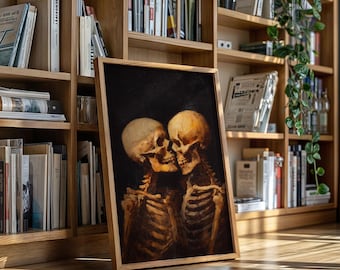 May include: A framed artwork featuring two skeletons embracing, set against a dark background. The skeletons are depicted in shades of beige and brown, with visible rib cages and skulls. The artwork is displayed on a wooden floor in front of a bookshelf.