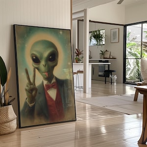 May include: Framed art print featuring a green alien in a suit, red bow tie, and peace sign gesture. The alien has large black eyes and a tongue sticking out. The background is a light blue with a halo effect.
