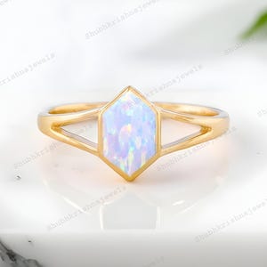 May include: A gold ring with a hexagonal, iridescent opal center stone. The ring has a split shank design, with the band splitting into two delicate lines on either side of the opal. The opal displays a range of colors.
