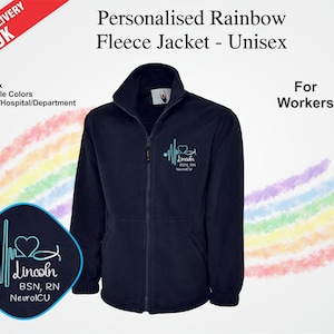 Puede incluir: Chaqueta polar azul marino con cremallera completa y cuello alto. Tiene un diseño bordado en azul claro y un parche con texto y un diseño en forma de corazón. El texto "Personalised Rainbow Fleece Jacket - Unisex" está en la parte superior.