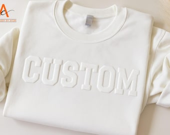 May include: White sweatshirt with the word "CUSTOM" in raised lettering.