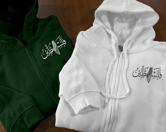 May include: Two zippered hoodies, one green and one white, with the Arabic phrase "Walid Ibn Walid" embroidered on the front. The phrase is in white on the green hoodie and in black on the white hoodie.