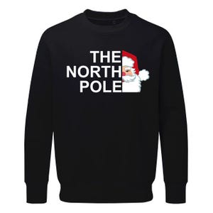May include: Black sweatshirt with white text that reads "THE NORTH POLE" and a cartoon image of Santa Claus peeking out from the right side of the text.