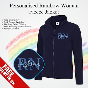 May include: Navy blue fleece jacket with a full zip and a high collar. The jacket has the embroidered name "Ashton" above the initials "RN" in a script font. The text "Personalised Rainbow Woman Fleece Jacket" is at the top.