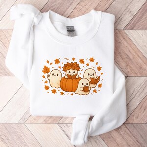 Peut inclure: Sweat-shirt blanc avec un motif sur le th&egrave;me de l'automne. Le motif repr&eacute;sente quatre fant&ocirc;mes de dessins anim&eacute;s, une citrouille et des feuilles d'automne. Un fant&ocirc;me est &agrave; l'int&eacute;rieur de la citrouille, et les autres lisent des livres ou tiennent une tasse.