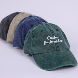 Könnte beinhalten: Vier Baseballkappen in verschiedenen Farben, darunter grün, blau, beige und grau. Die grüne Kappe hat den Text "Custom Embroidery" auf der Vorderseite gestickt.