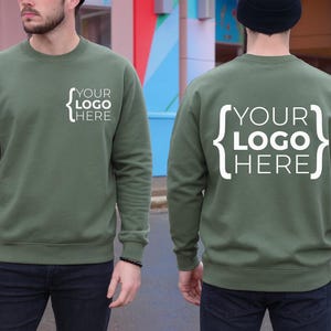 Op de afbeelding: Olijfgroene sweatshirt met de witte tekst "YOUR LOGO HERE" in een haakjesontwerp. Het sweatshirt heeft een ronde hals en wordt van voren en van achteren getoond. Een casual kledingstijl.
