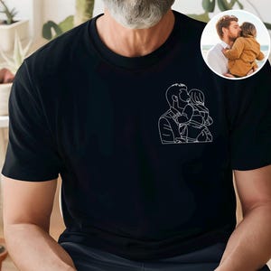 以下が含まれることがあります： 親が子供にキスをしている白い線画が特徴の黒いTシャツ。右上にある小さな円形の画像は、親が子供にキスをしている様子を示しています。このシャツは柔らかい素材で作られています。