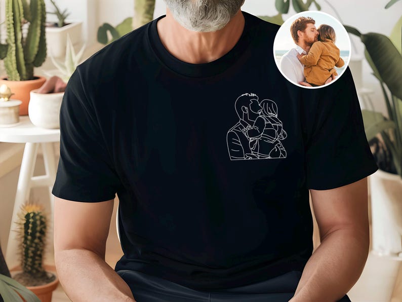 以下が含まれることがあります： 親が子供にキスをしている白い線画が特徴の黒いTシャツ。右上にある小さな円形の画像は、親が子供にキスをしている様子を示しています。このシャツは柔らかい素材で作られています。