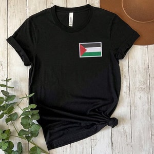 Könnte beinhalten: Schwarzes T-Shirt mit einem palästinensischen Flaggen-Motiv auf der Vorderseite. Die Flagge ist rot, grün, schwarz und weiß.