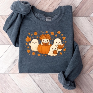 Peut inclure: Un sweat-shirt bleu fonc&eacute; avec un motif sur le th&egrave;me de l'automne. Le motif comprend trois fant&ocirc;mes amicaux, une citrouille et des feuilles d'automne. Les fant&ocirc;mes lisent des livres et tiennent des tasses, cr&eacute;ant un design chaleureux et saisonnier.