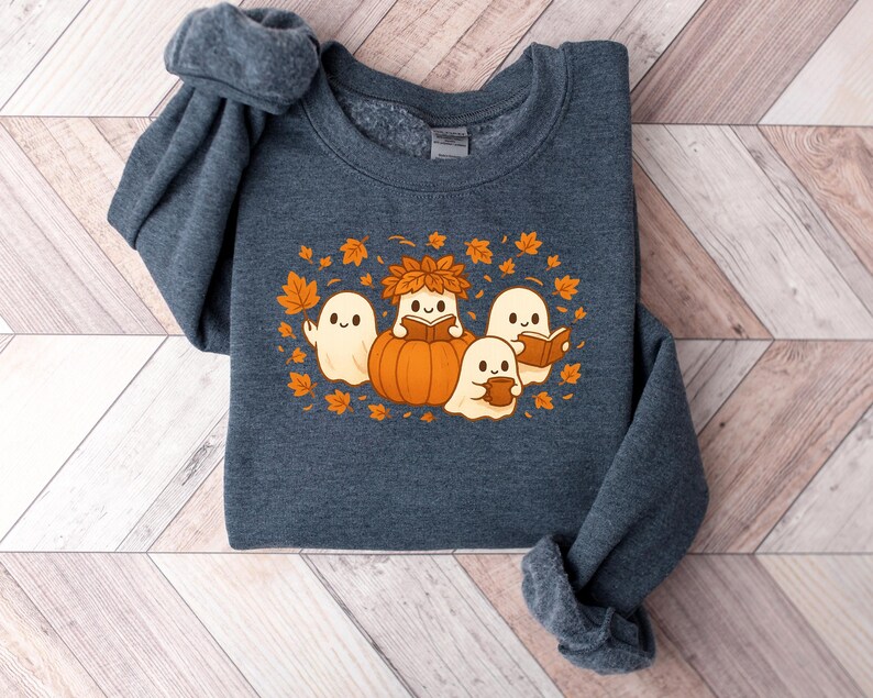 Peut inclure: Un sweat-shirt bleu fonc&eacute; avec un motif sur le th&egrave;me de l'automne. Le motif comprend trois fant&ocirc;mes amicaux, une citrouille et des feuilles d'automne. Les fant&ocirc;mes lisent des livres et tiennent des tasses, cr&eacute;ant un design chaleureux et saisonnier.