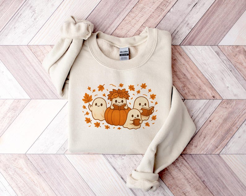 Peut inclure: Sweat-shirt cr&egrave;me avec un motif sur le th&egrave;me de l'automne. Le motif comprend des fant&ocirc;mes de dessins anim&eacute;s, une citrouille et des feuilles d'automne dans des tons orange et marron. Le sweat-shirt a un col rond et des manches longues.