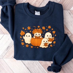 Peut inclure: Sweat-shirt bleu marine avec un motif sur le th&egrave;me de l'automne. Le motif comprend des fant&ocirc;mes de dessins anim&eacute;s, une citrouille et des feuilles d'automne orange et marron. Les fant&ocirc;mes lisent des livres et tiennent des tasses. Un v&ecirc;tement de saison confortable.