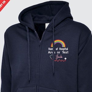 Könnte beinhalten: Marineblaue Kapuzenjacke mit Reißverschluss, verziert mit einem Regenbogen und dem Text "Name of Hospital Area or Text" und "Jack". Die Kapuzenjacke hat eine Kapuze und einen Reißverschluss vorne. Ein Stethoskop und eine Herzschlag-Grafik sind ebenfalls vorhanden.