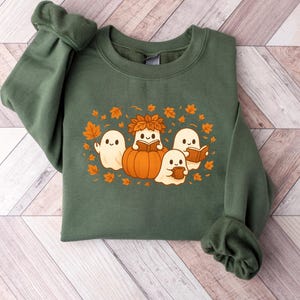 Peut inclure: Sweat-shirt vert avec un motif sur le th&egrave;me de l'automne. Le motif comprend quatre fant&ocirc;mes de dessins anim&eacute;s, une citrouille et des feuilles d'automne. Les fant&ocirc;mes lisent des livres et tiennent une tasse. Le sweat-shirt est en mati&egrave;re douce.