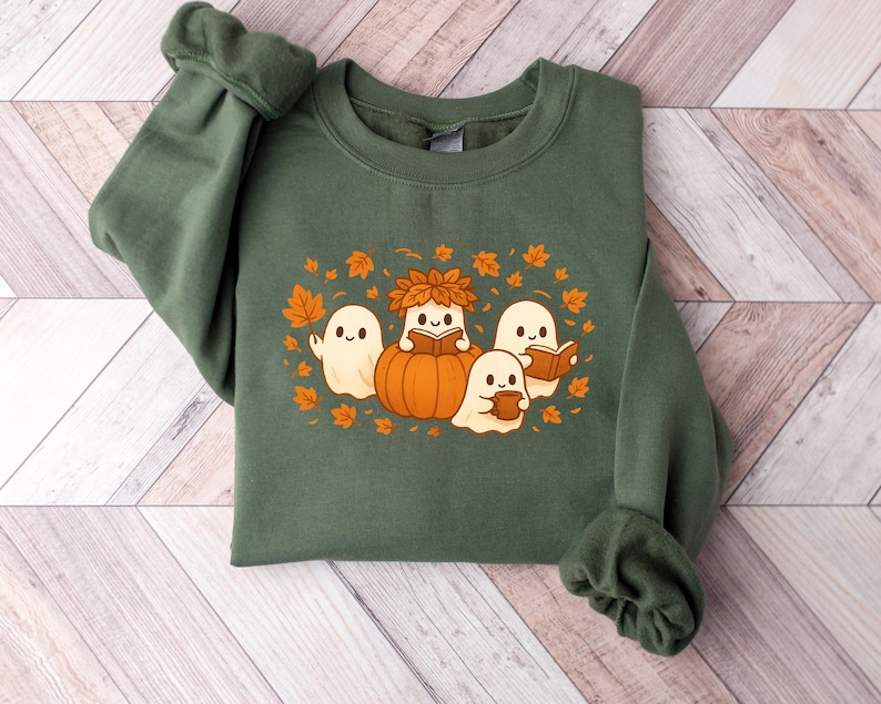Peut inclure: Sweat-shirt vert avec un motif sur le th&egrave;me de l'automne. Le motif comprend quatre fant&ocirc;mes de dessins anim&eacute;s, une citrouille et des feuilles d'automne. Les fant&ocirc;mes lisent des livres et tiennent une tasse. Le sweat-shirt est en mati&egrave;re douce.
