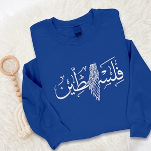 May include: A royal blue sweatshirt with a white Arabic calligraphy design featuring the word "Palestine" and a stylized image of the Palestinian flag.