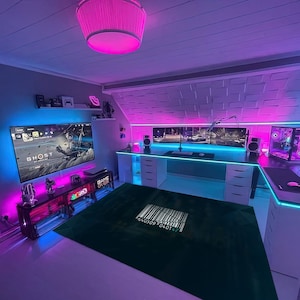 Op de afbeelding: Een gamer-opstelling met een grote tv, een computermonitor en een wit bureau met laden. De kamer is versierd met roze en blauwe neonlichten. Het bureau heeft een groen tapijt met een barcode-ontwerp en de woorden "GAME OVER" erop.