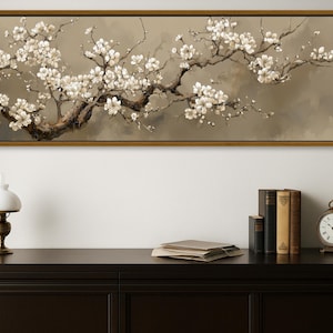 May include: A framed canvas print depicting a flowering tree branch with white blossoms. The artwork is set against a muted backdrop. A dark brown cabinet below holds a lamp, books, and a clock, creating a classic aesthetic.