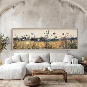Op de afbeelding: Een panoramisch landschapsschilderij in een houten lijst met een veld vol wilde bloemen in blauwe en rode tinten tegen een gedempte gouden en donkergroene achtergrond. Het kunstwerk toont hoog gras en verspreide bloemstengels in een weide.