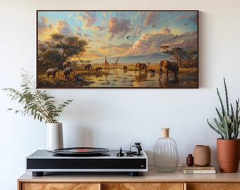May include: A rectangular framed wall art print depicting a savanna landscape at sunset with elephants and giraffes near a watering hole. The scene features warm golden light, scattered clouds, and acacia trees, mounted above a wooden cabinet.