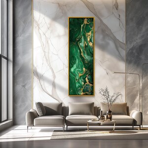 May include: A vertical rectangular wall art piece featuring a swirling abstract pattern of deep emerald green and metallic gold veins, encased in a thin gold frame, displayed on a white marble wall above a light gray sectional sofa and coffee table.