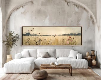 Puede incluir: Un cuadro panorámico de paisaje que muestra un campo de trigo dorado bajo un cielo suave y brumoso. La escena incluye hierbas altas y secas, cabezas de semillas oscuras y grupos de flores silvestres de color rosa suave, en un marco de madera.