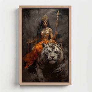 May include: A framed artwork depicts a woman in gold attire, seated atop a white tiger. She holds a spear, and the background is a blend of dark grays and blacks. The artwork is framed in a light-colored wood.